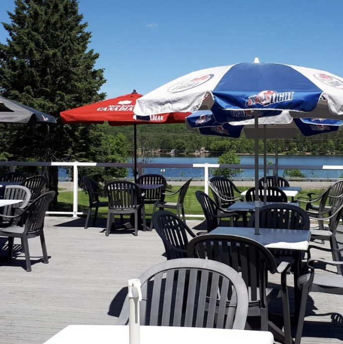 A patio with chair, tables, and umbrellas overlooking a lake.